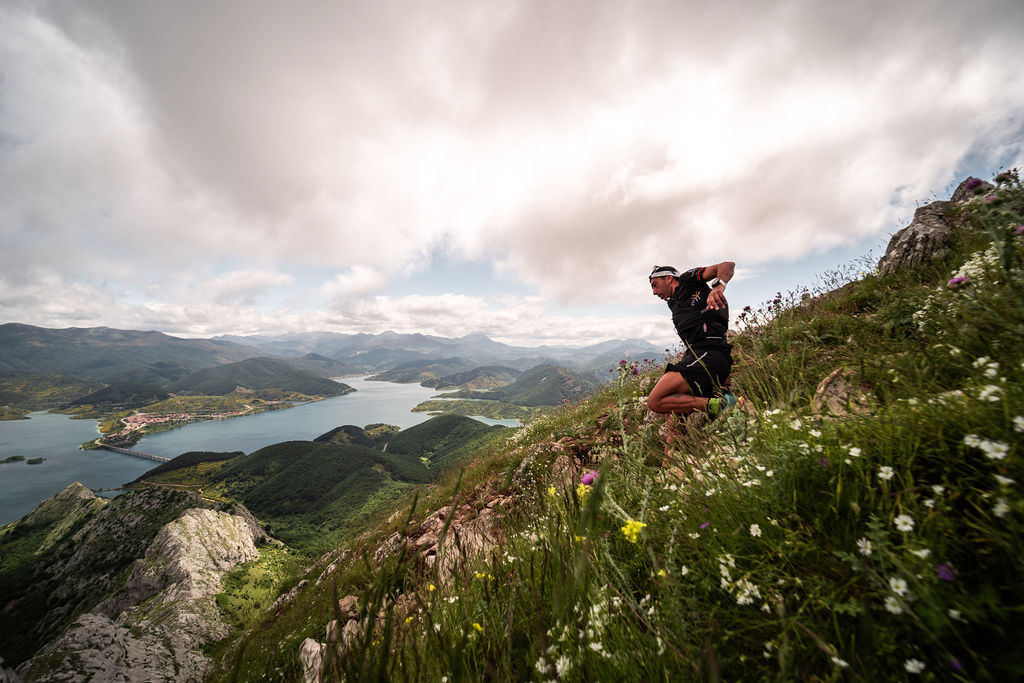 Corredor de trail running descendiendo una ladera técnica de Riaño Trail Run, con vistas panorámicas al embalse de Riaño y las montañas bajo un cielo nublado